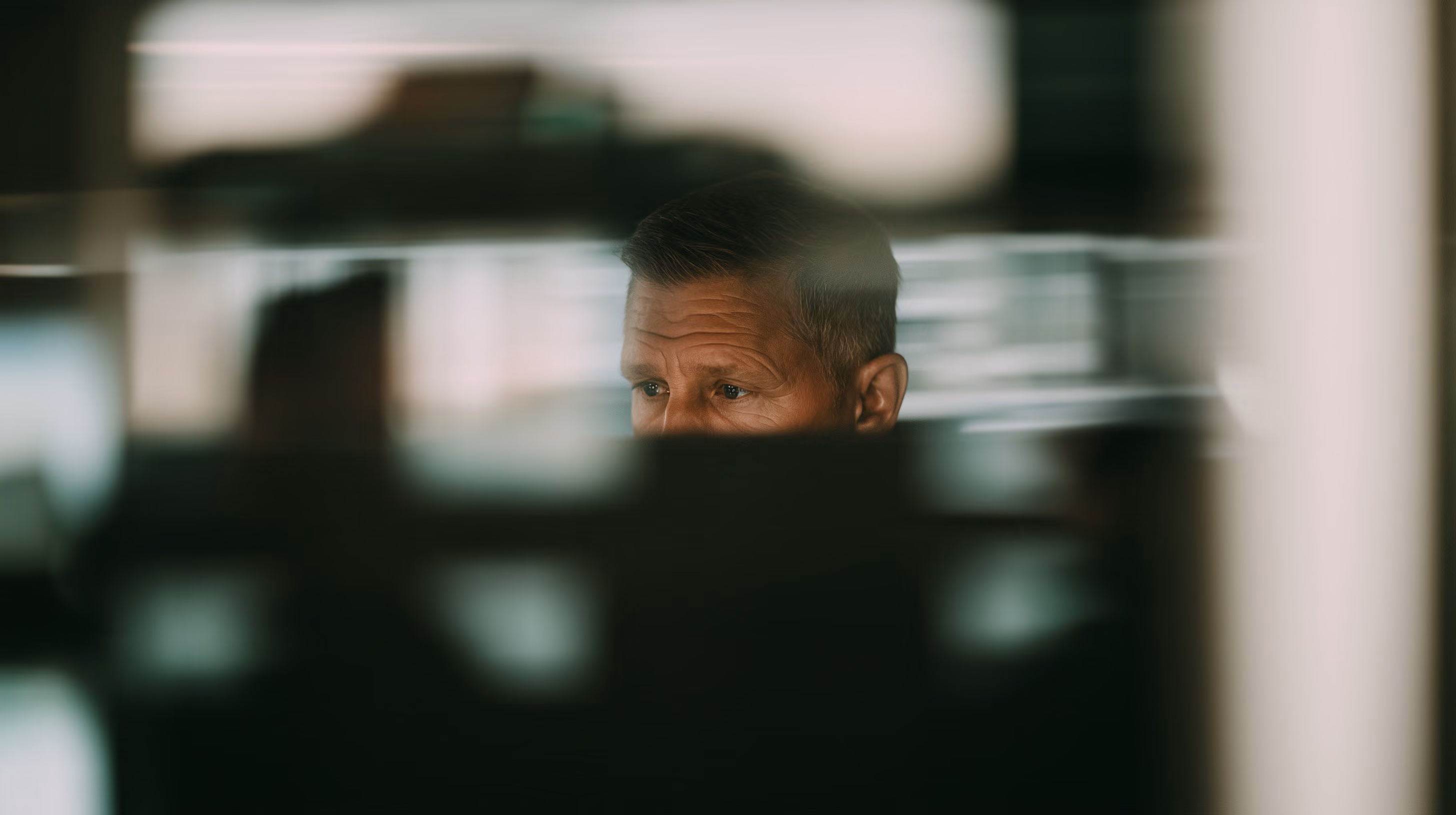A darkened scene, with a face behind reflections in glass.